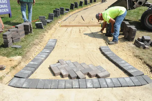 A crew member laying brick pavers by hand