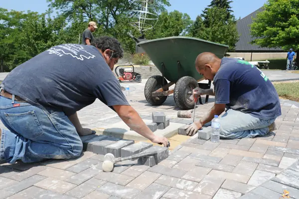 Two crew members installing brick pavers together