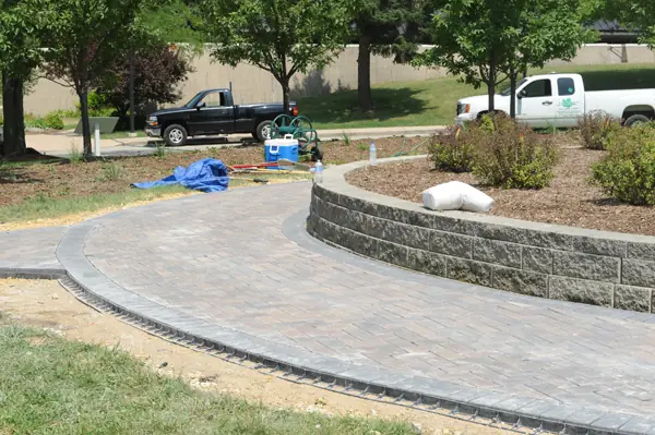 Curved stone retaining wall beside a brick paver walkway, with the company truck parked at the kerb